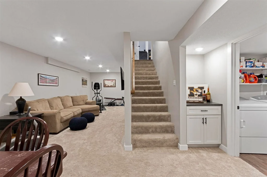 Finished basement recreation room with sectional sofa, game table, laundry nook and staircase to the main level, a Pinnacle Projects basement remodel in Mid-Missouri.