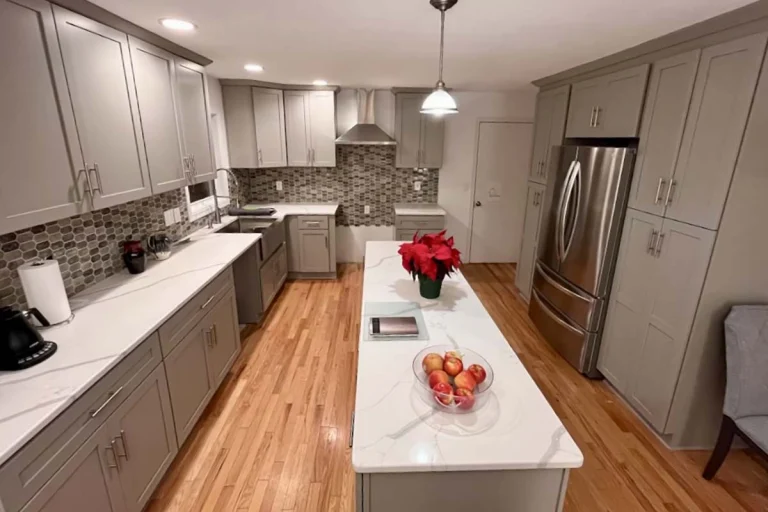 Kitchen with gray cabinets, a stainless steel refrigerator and a white island holding apples and a red poinsettia