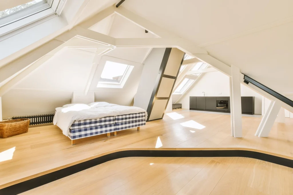 Bright attic room with a checkered bed, skylights, white beams, wood floors and dark kitchen cabinets
