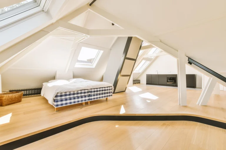 Bright attic room with a checkered bed, skylights, white beams, wood floors and dark kitchen cabinets