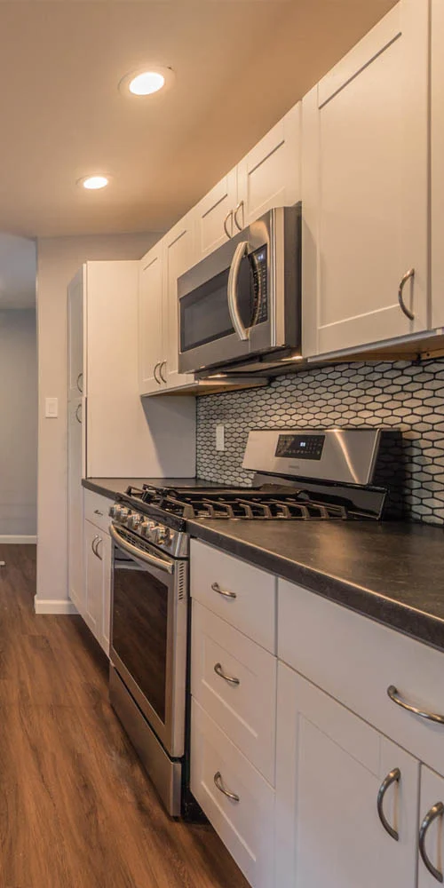 Kitchen with white cabinets, stainless steel microwave and gas range, dark countertops and hexagonal tile backsplash