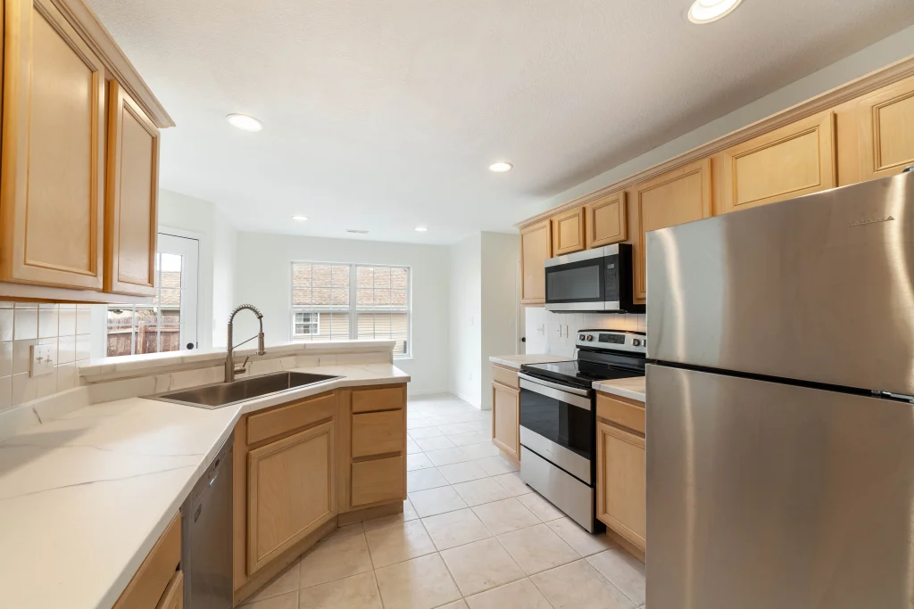 Kitchen with light wood cabinets, white counters, a double sink, stainless steel refrigerator, stove and microwave