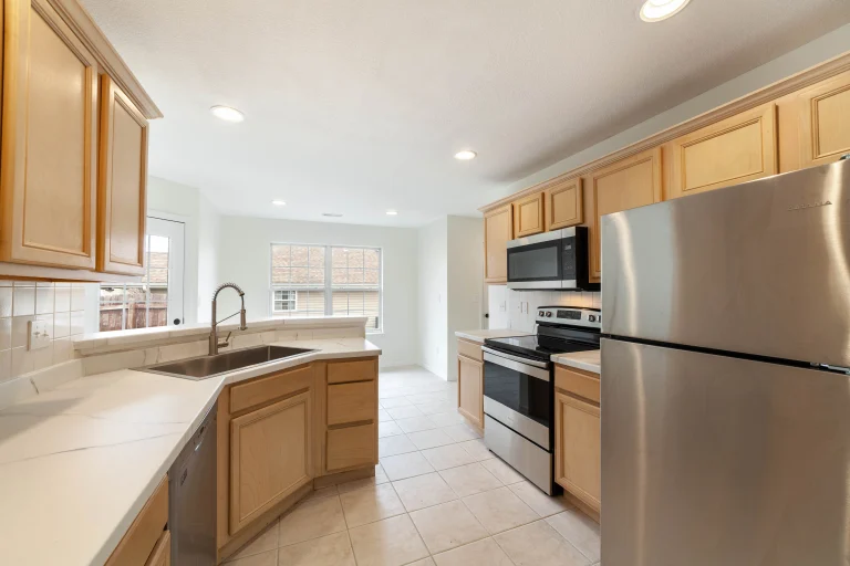 Kitchen with light wood cabinets, white counters, a double sink, stainless steel refrigerator, stove and microwave