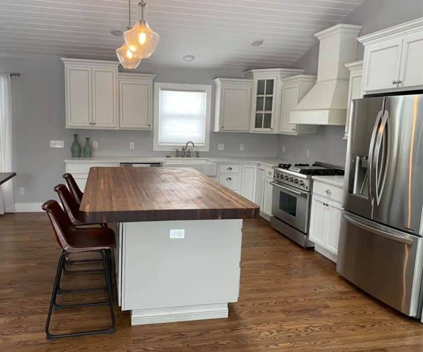 Kitchen with white cabinets, wood-topped island, three stools, pendant lights and stainless appliances