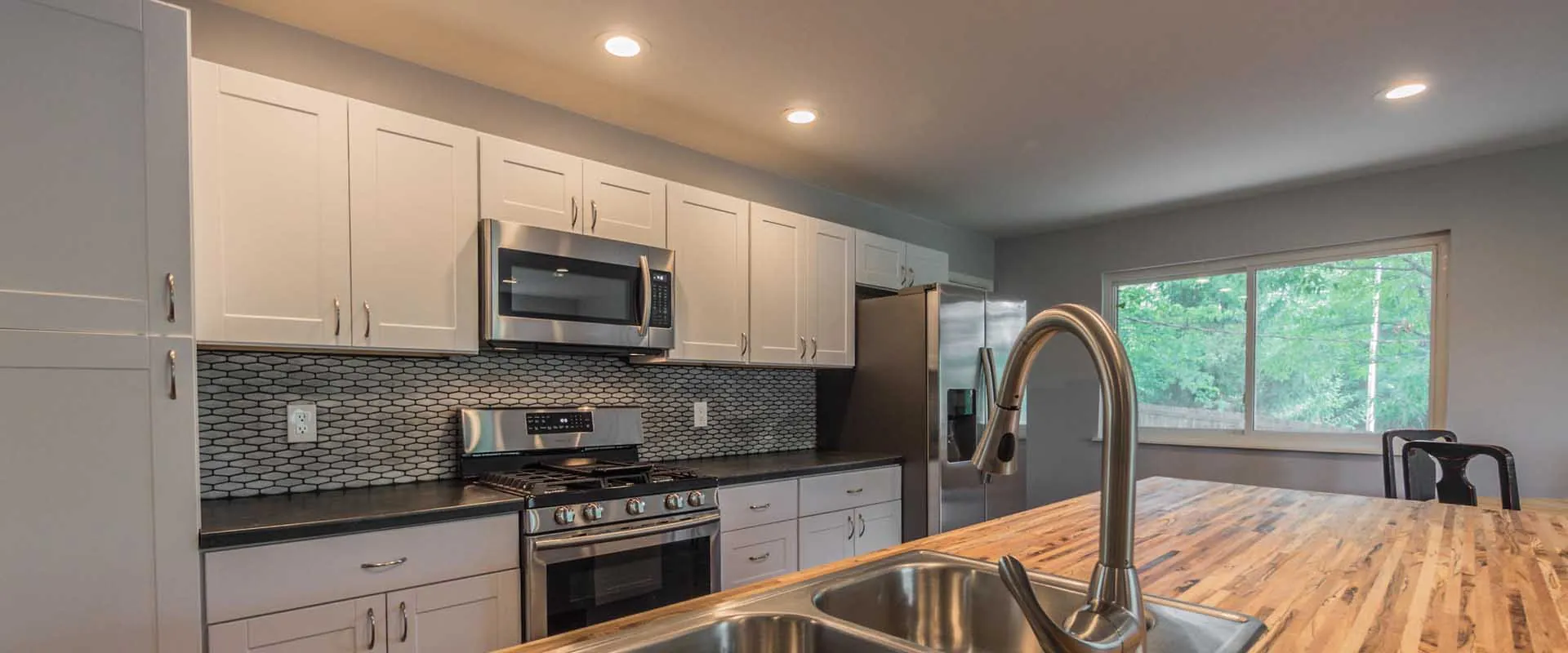 Kitchen with white cabinets, stainless steel appliances, tiled backsplash and a wood island with a sink and tall faucet