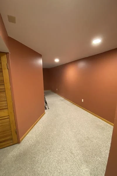 Narrow room with reddish-brown walls, beige carpet, recessed lights, and a wooden louvered door
