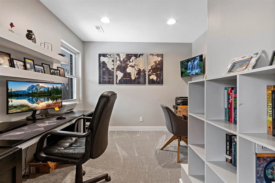 Office with desk, monitor, black chair, map art, and white shelves