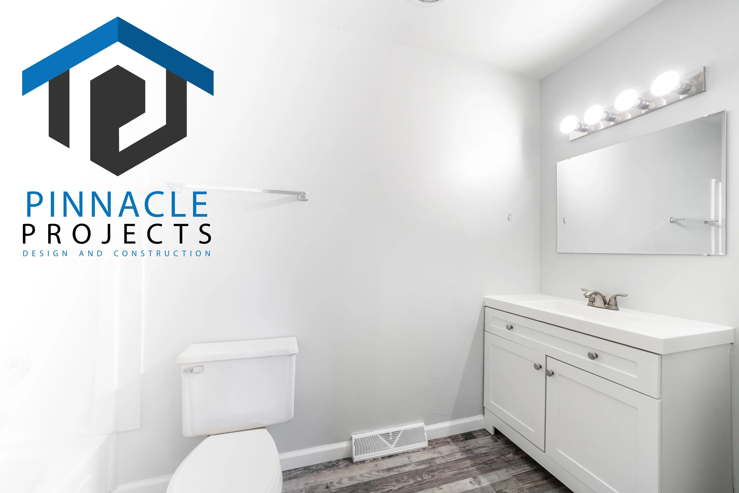 White bathroom with toilet, vanity, mirror and lights; text “PINNACLE PROJECTS DESIGN AND CONSTRUCTION”