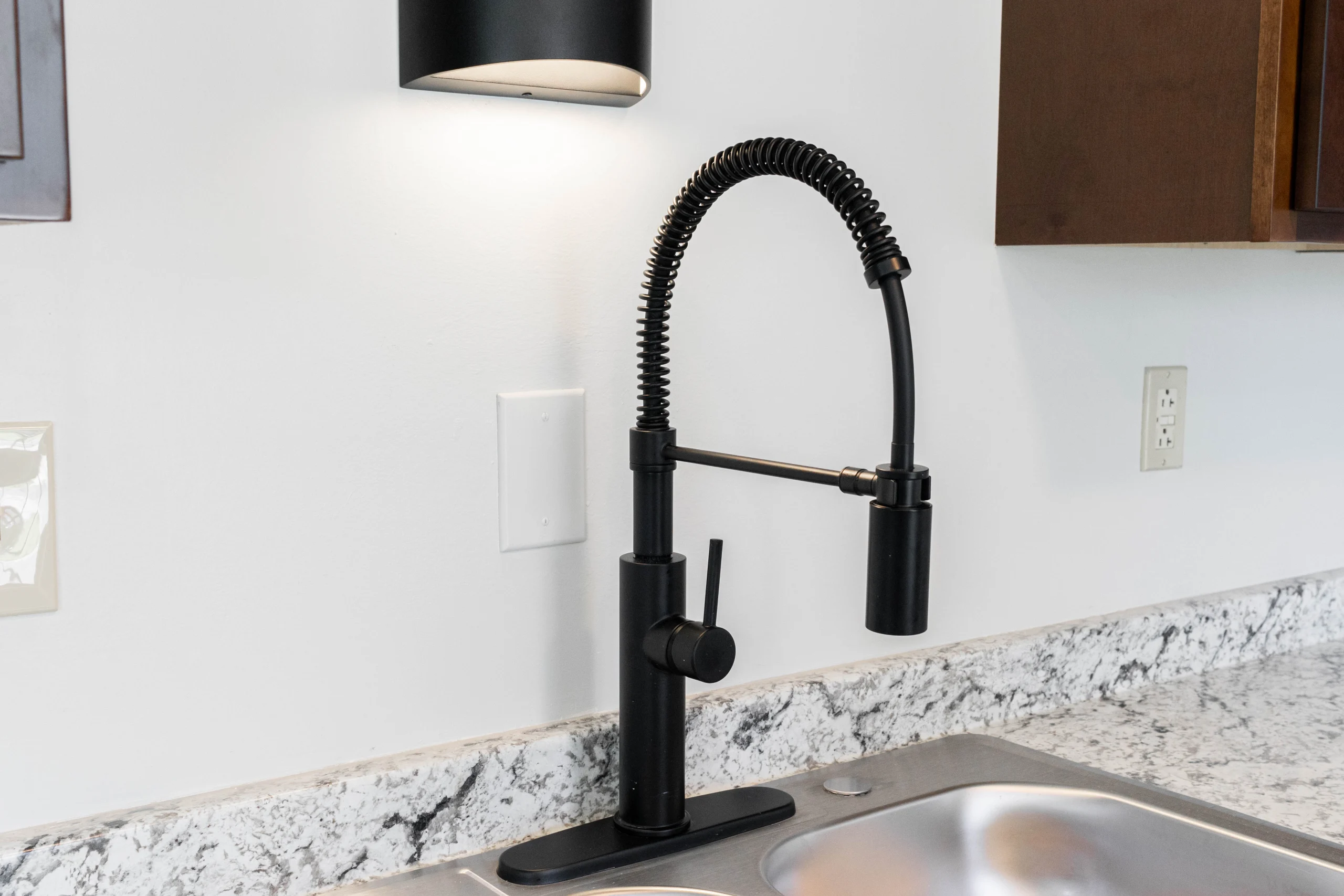 Black spring-coil faucet above a stainless steel sink, with a marble-patterned counter and backsplash