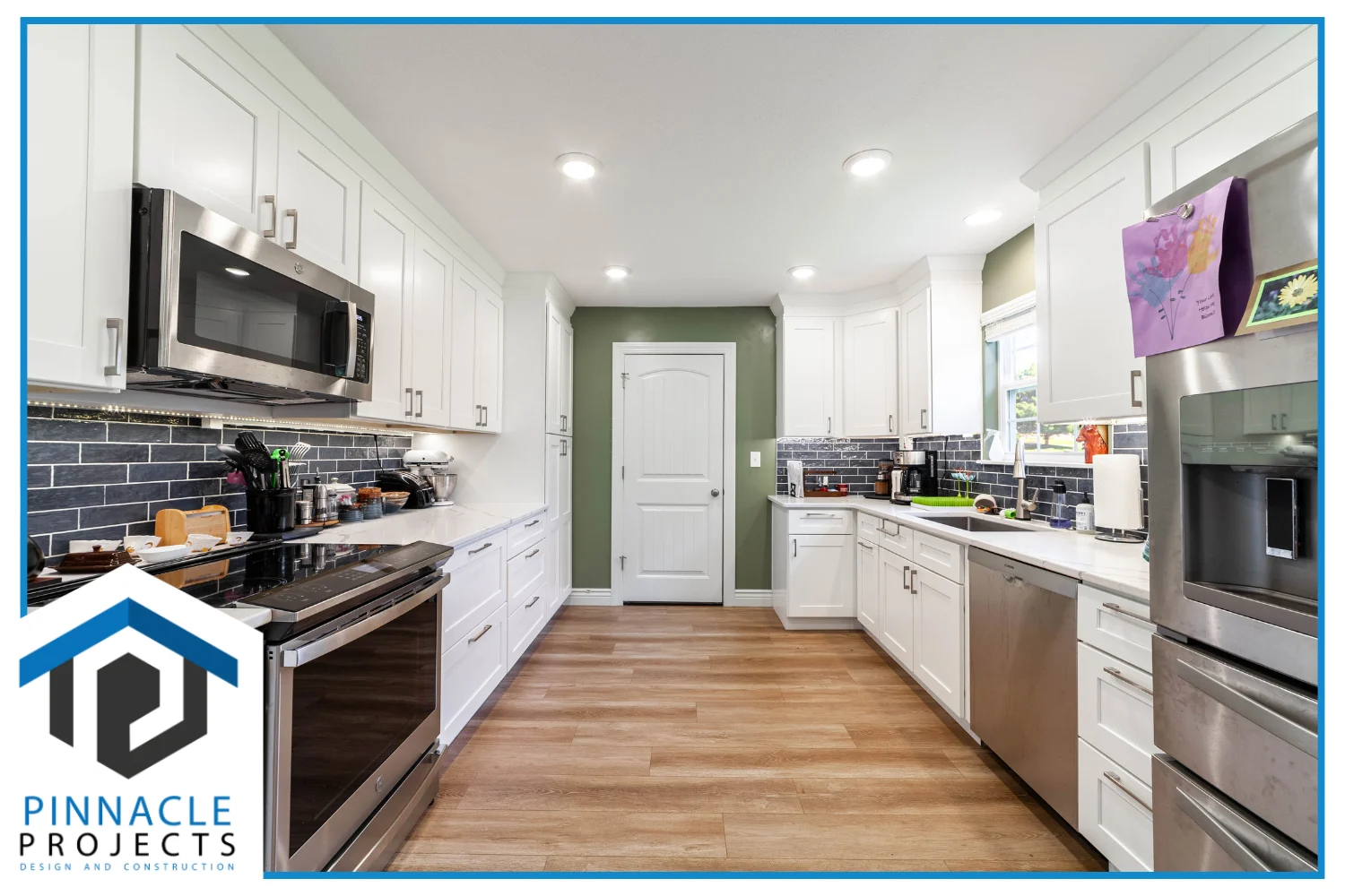 White kitchen with stainless appliances, dark tile backsplash, wood floor; logo reads “PINNACLE PROJECTS”