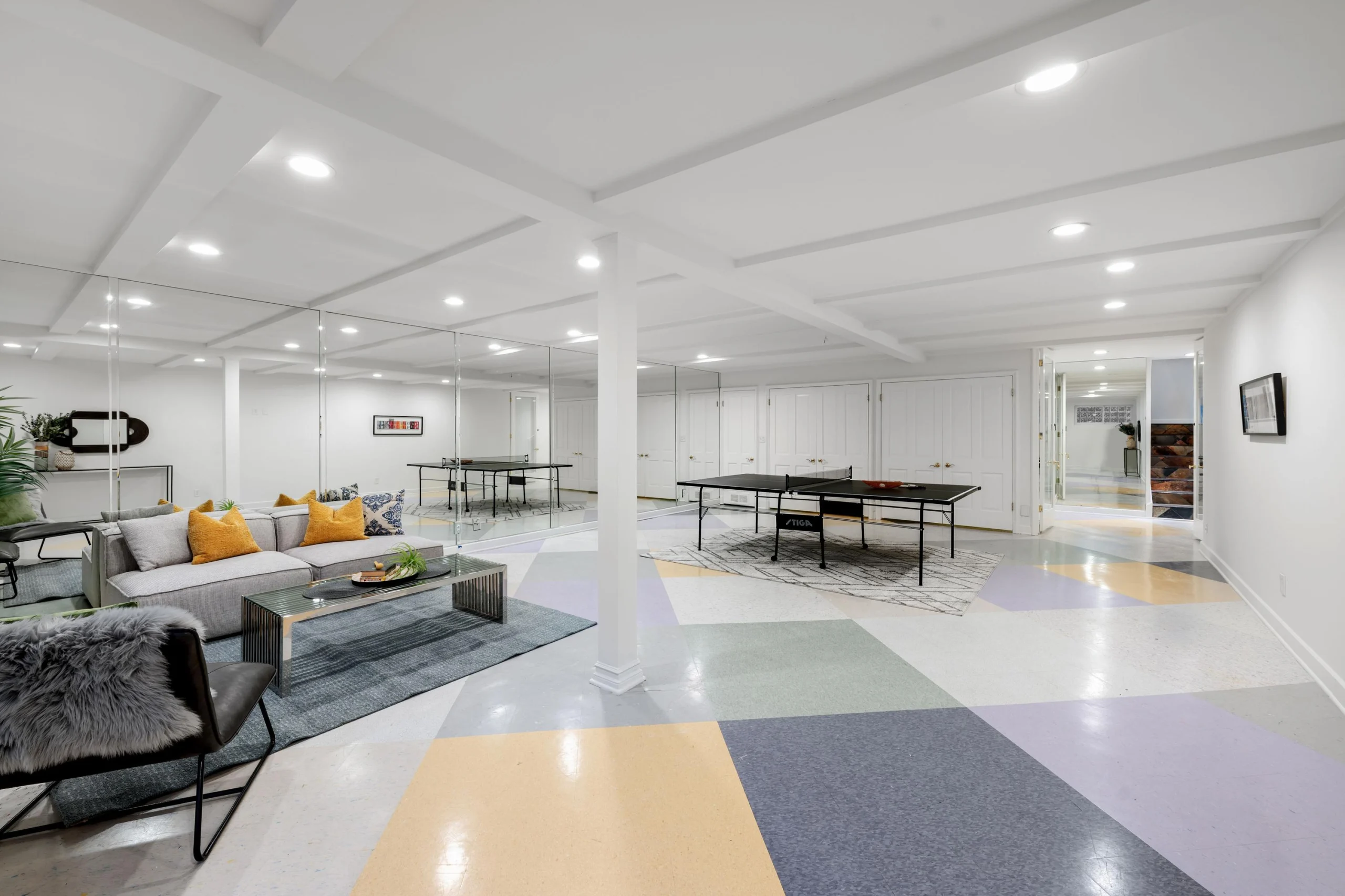 Bright room with mirrored walls, a sofa, chairs, coffee table, ping-pong table, and multicolored geometric flooring