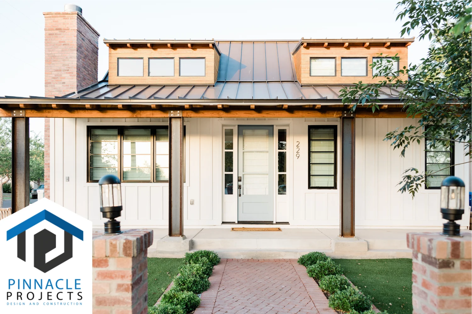 White house with metal roof, dormers, timber porch and brick path; “PINNACLE PROJECTS” logo