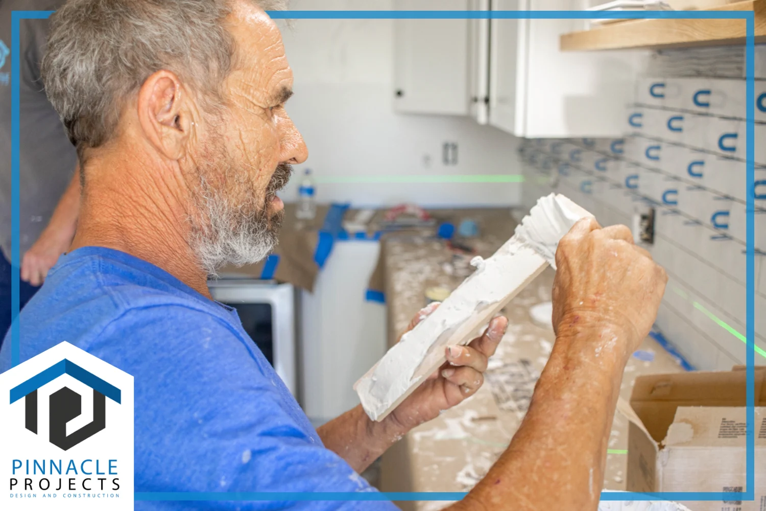 Man holding tools with white paste in a kitchen; logo reads “PINNACLE PROJECTS DESIGN AND CONSTRUCTION”