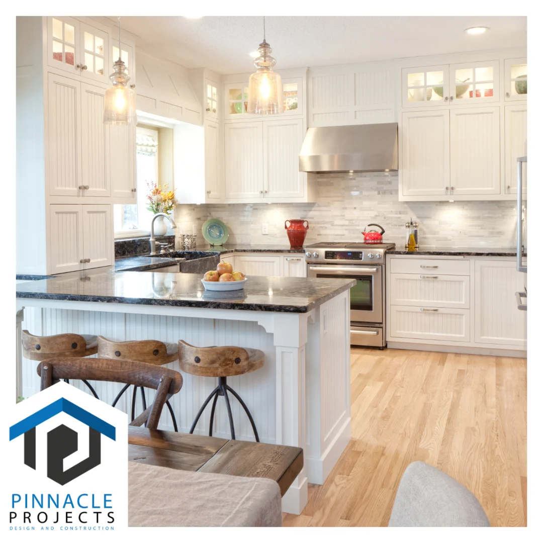 White kitchen with an island, wooden stools, pendant lights, stove, and hood; logo reads “PINNACLE PROJECTS”
