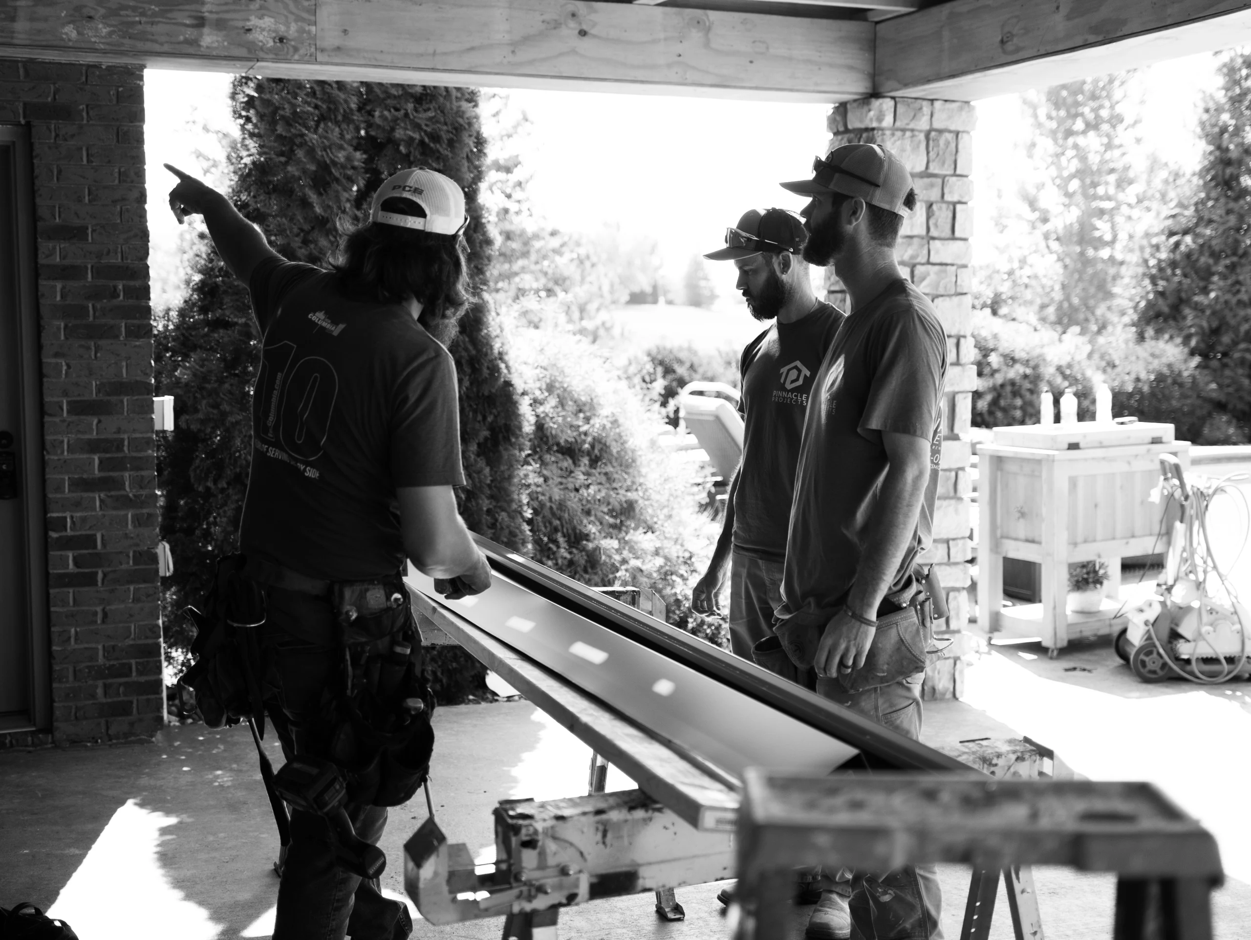 Black-and-white photo of three men beside a long panel on sawhorses; one points