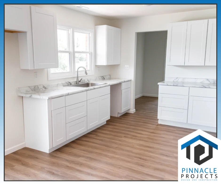 White kitchen with marble-look counters and wood-look floor; logo “PINNACLE PROJECTS DESIGN AND CONSTRUCTION”